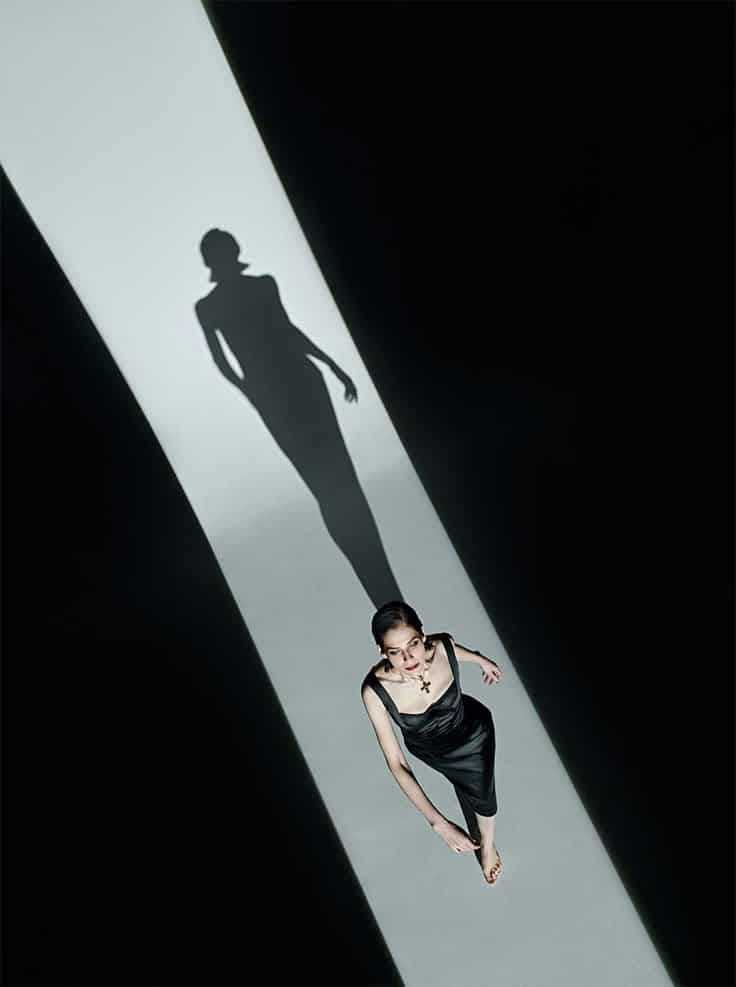 Woman in black dress walking on lit pathway, casting long shadow. Elegant style and dramatic lighting.