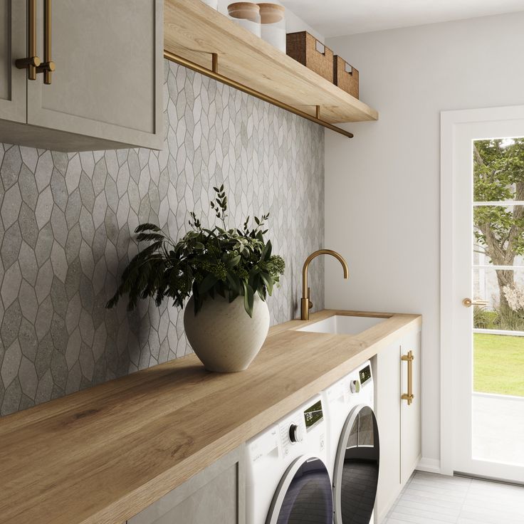 Modern laundry room with washer and dryer, wooden countertop, geometric backsplash, and potted plant.