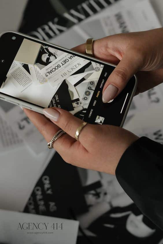 Person holding a smartphone taking a photo of stylish black and white print media with text Agency 414, close-up.