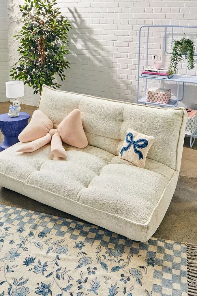 Cozy living room with a cream sofa, decorative pillows, blue side table, and a lush potted plant.