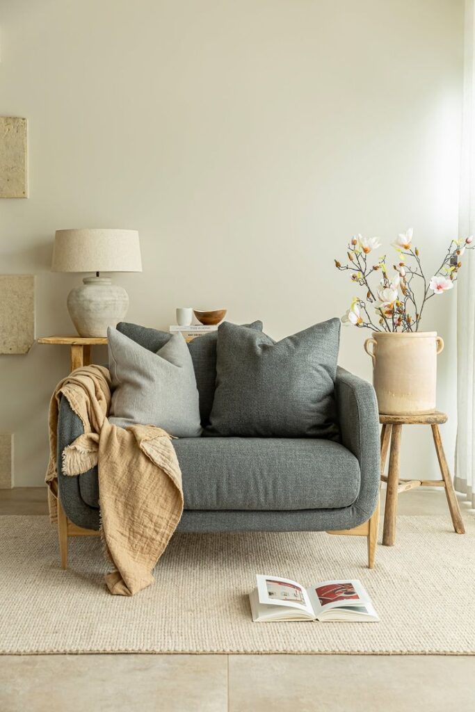 Modern cozy living room with gray sofa, pillows, and a throw blanket, alongside a stylish lamp and floral decor.