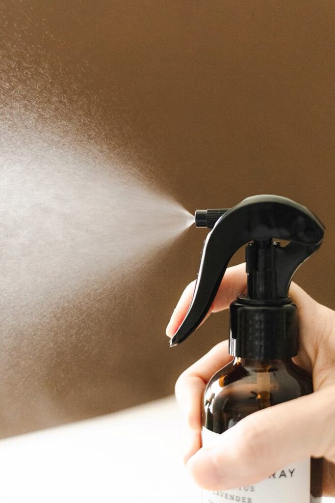 Hand holding spray bottle with mist, brown background, close-up.