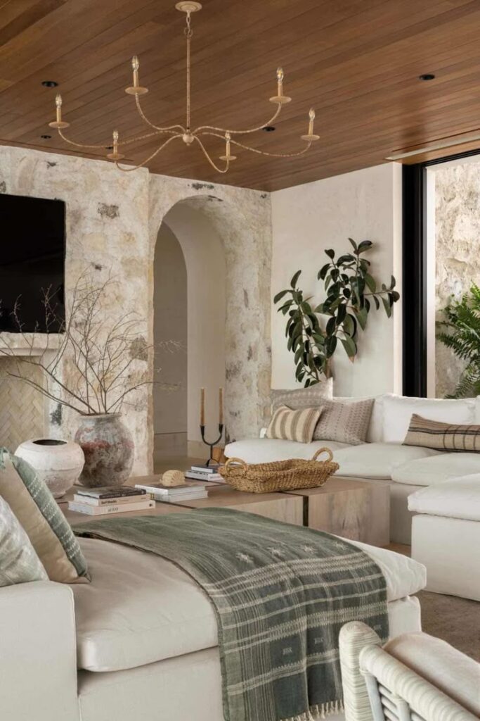 Modern living room with white sofas, stone wall, wooden ceiling, and decorative plants for a cozy ambiance.