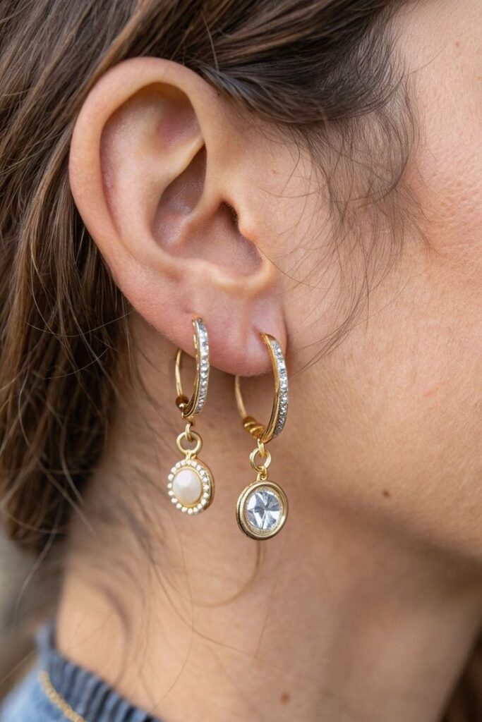Close-up of a woman's ear wearing elegant gold and gemstone hoop earrings.