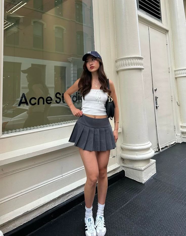 Woman in a sporty outfit and cap poses outside Acne Studios, blending fashion and urban style effortlessly.