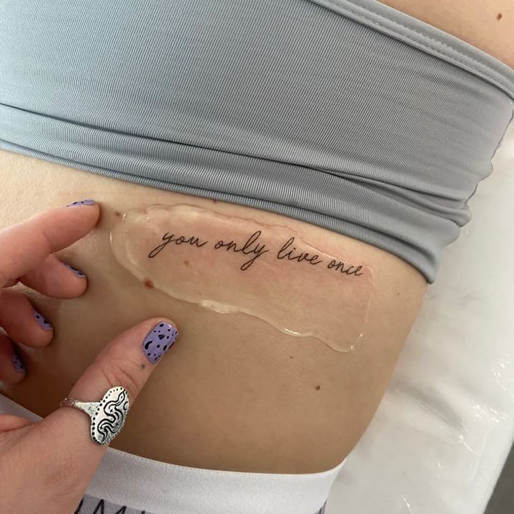 Close-up of a fresh tattoo reading you only live once on a person's side, covered with protective film.
