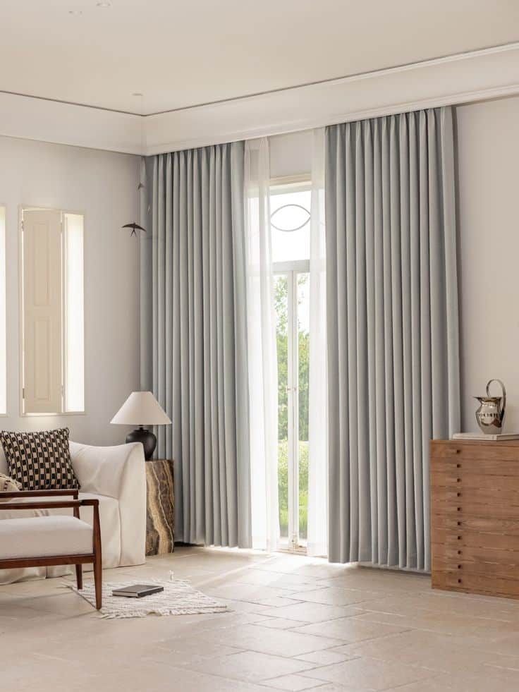 Modern living room with elegant gray curtains, cozy seating, and natural light from large window.