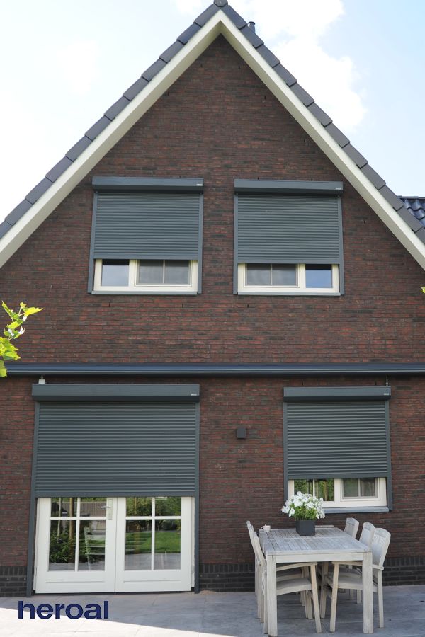 Thanks to unlimited design possibilites heroal roller shutters can be customized to your individual requirements_ Modern brick house with closed roller shutters, outdoor dining set on patio, and clear blue sky. | Sky Rye Design Modern brick house with closed roller shutters, outdoor dining set on patio, and clear blue sky.