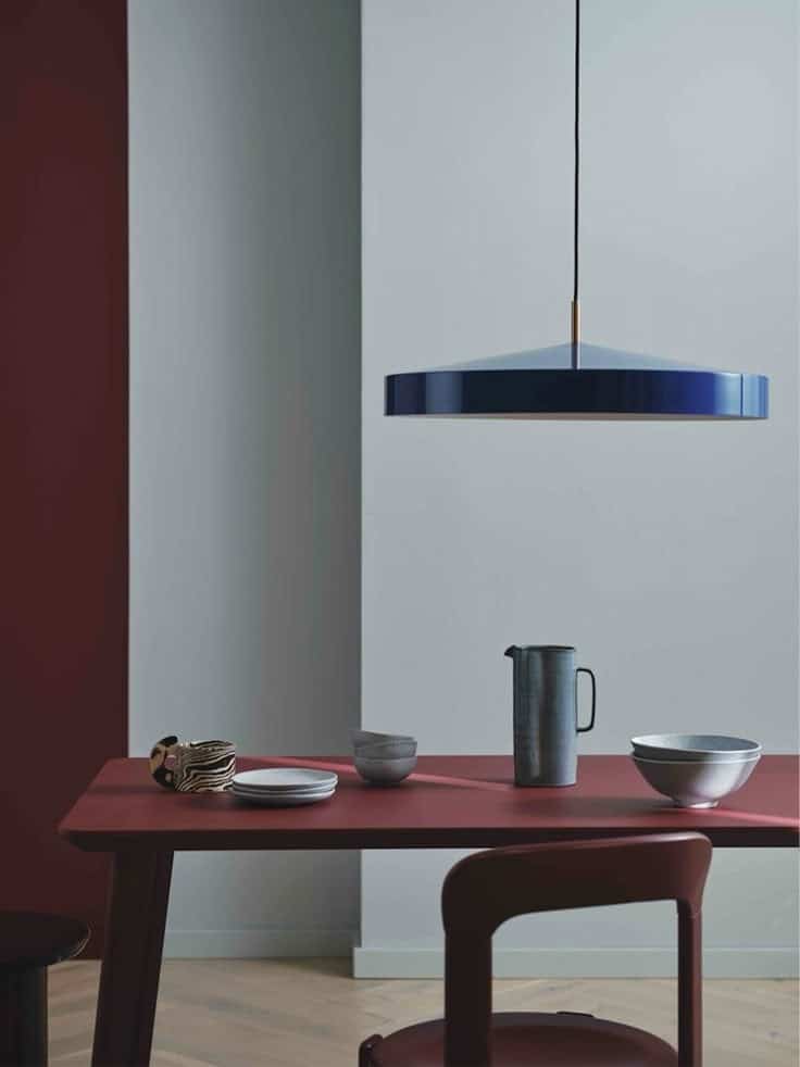 Modern dining area with minimalist red table, blue pendant light, and elegant dishware.
