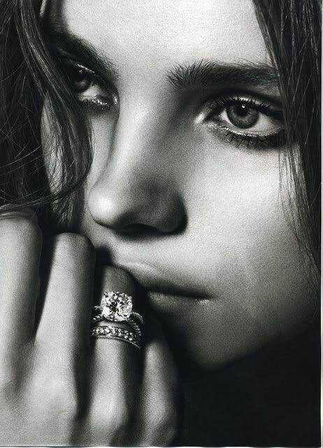 Black and white image of a woman's face focused on her thoughtful expression and sparkling diamond rings on her fingers.