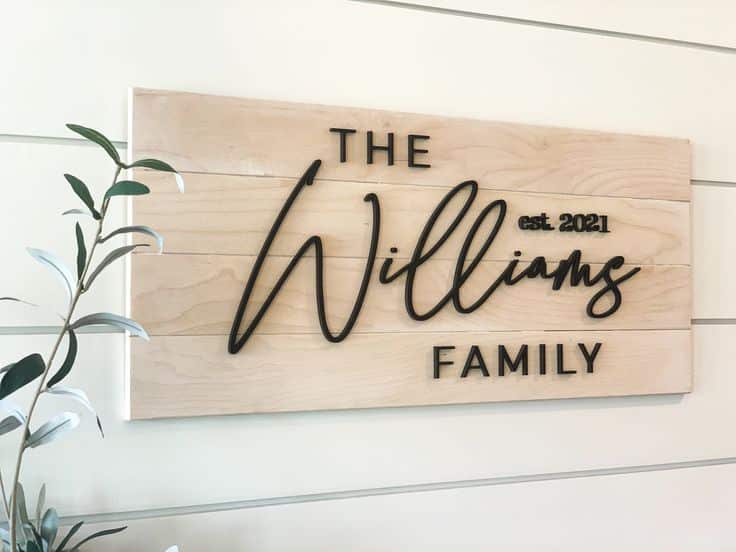 Wooden family name sign with The Williams Family, est. 2021 in stylish black font, beside indoor plant.