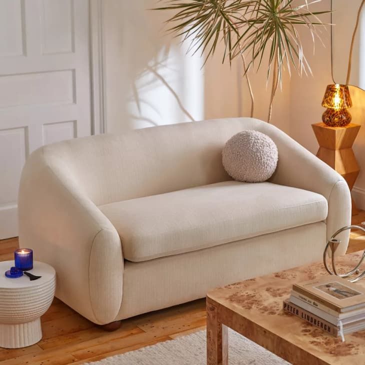 Cozy beige loveseat in a stylish living room with a plant, candle, and modern decor.