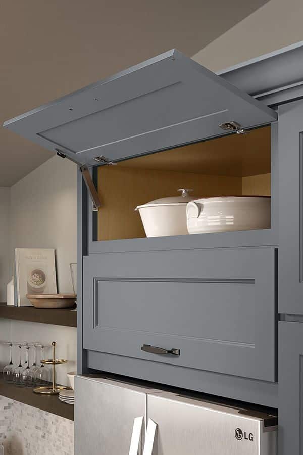 Gray kitchen cabinet with lift-up door revealing a white casserole dish inside, above an LG refrigerator.