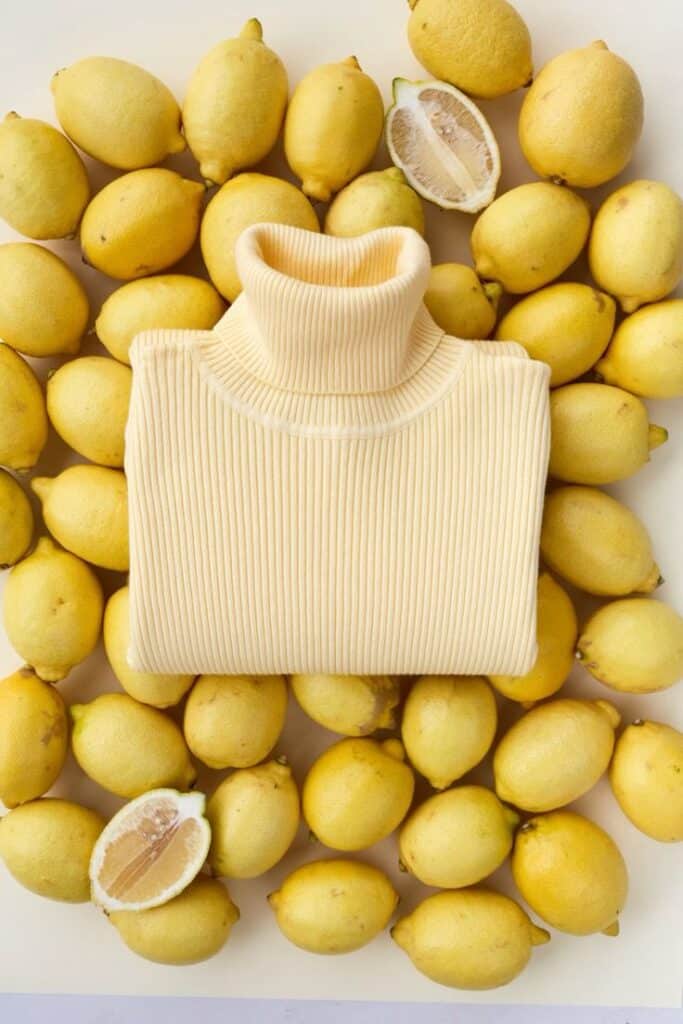 Cream turtleneck sweater surrounded by fresh lemons on a light background.