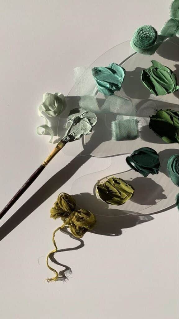 Paintbrush and green shades of paint on palette, creative art supplies arrangement in sunlight.