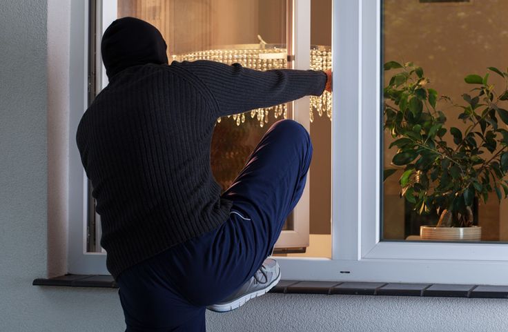 Travel Safety Tips and Advice for Worry-Free Travel Burglar in dark clothing climbing into a brightly lit house through an open window at night. | Sky Rye Design Burglar in dark clothing climbing into a brightly lit house through an open window at night.