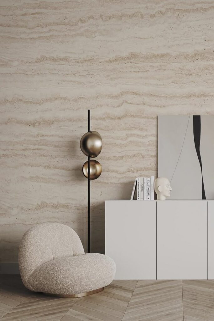 Modern living room with a beige armchair, abstract art, decorative objects, and a textured wall. Minimalistic interior design.