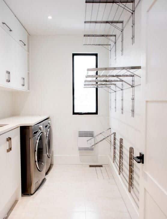 Modern laundry room with stacked appliances, wall-mounted drying racks, and white cabinetry for efficient storage.