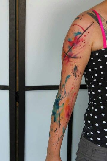 Watercolor-style abstract tattoo on a woman's arm, featuring vibrant colors and artistic splashes, wearing a polka-dot top.