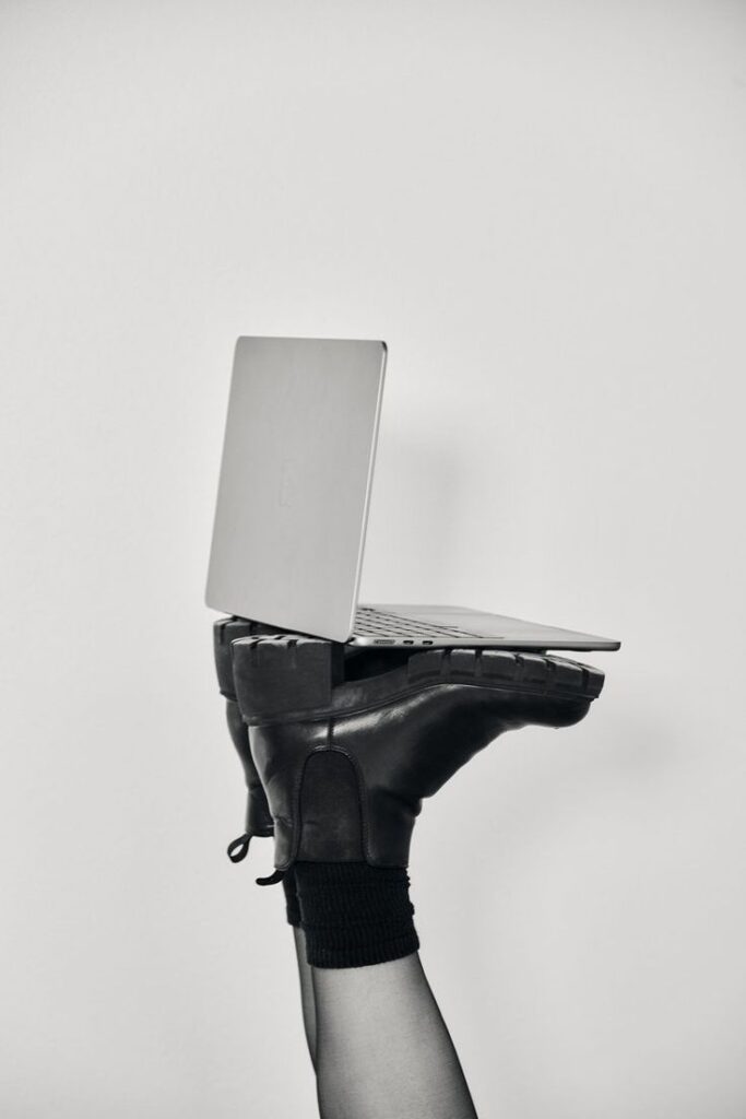 A laptop balanced on a booted foot, showcasing creativity and balance in black and white minimalistic style.