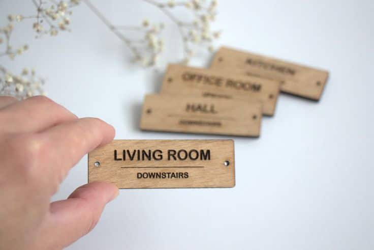 Wooden room labels for living room, kitchen, office, and hall, held in hand on white background.
