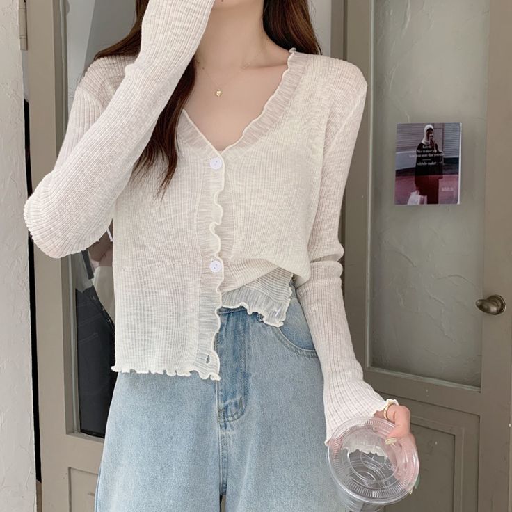 Woman in a stylish beige cardigan and jeans holding a clear cup indoors. Casual fashion outfit inspiration.