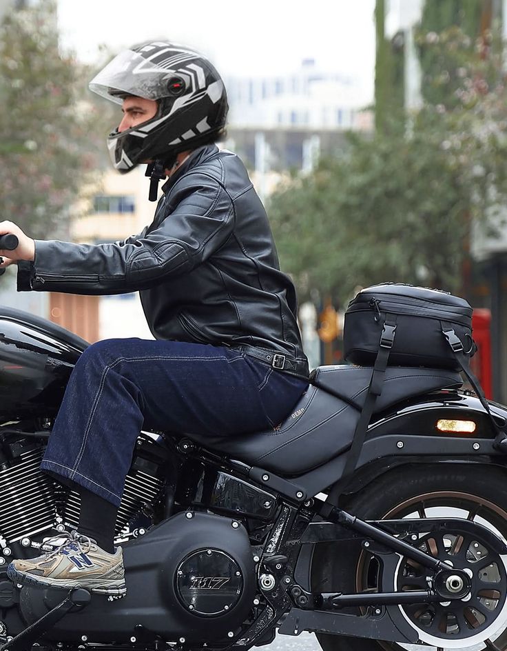 Person riding a black motorcycle, wearing a helmet and leather jacket, in an urban setting.