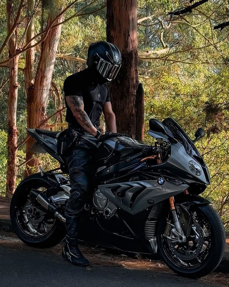 Rider in black gear with sleek motorcycle in a forest setting, showcasing adventure and style.