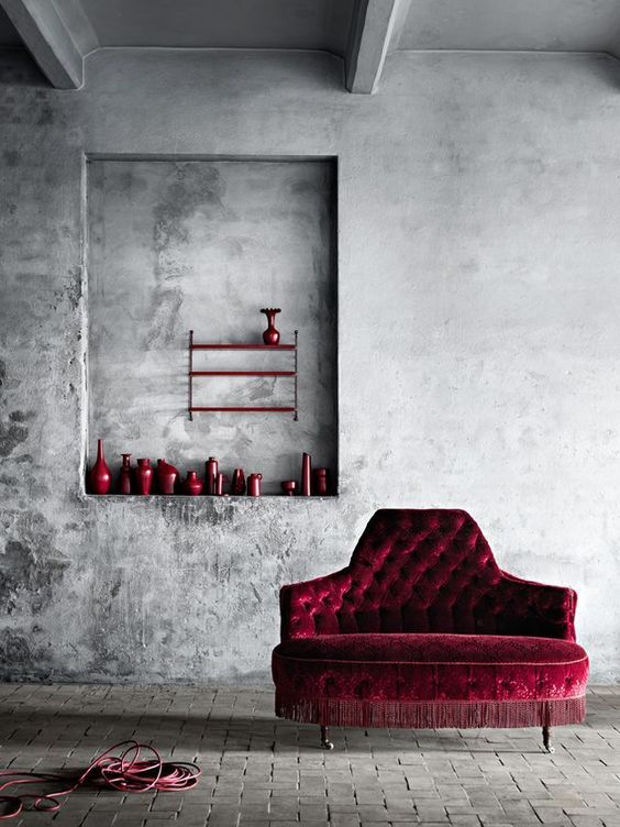 Vintage red velvet sofa with matching vases in a minimalist grey room, creating a bold contrast.