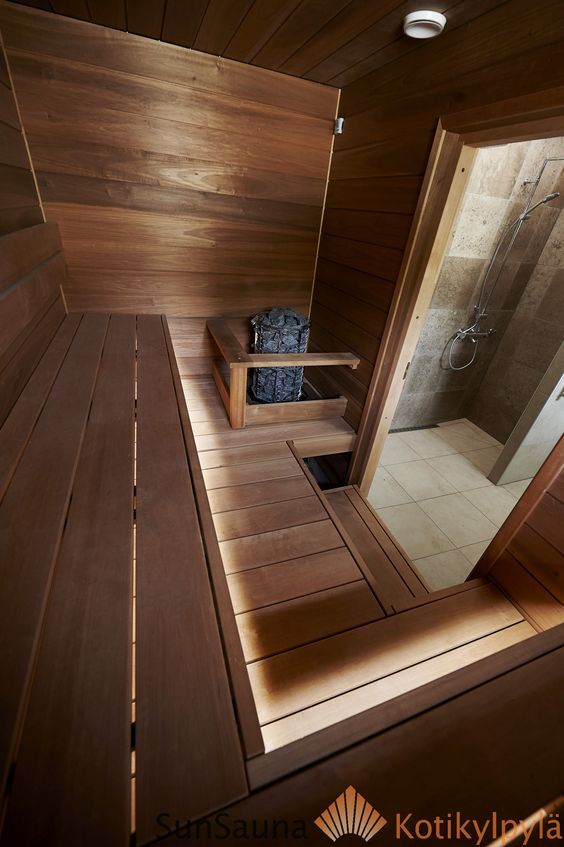Wooden sauna interior with shower view, featuring benches and a heater with rocks, evoking relaxation and warmth.