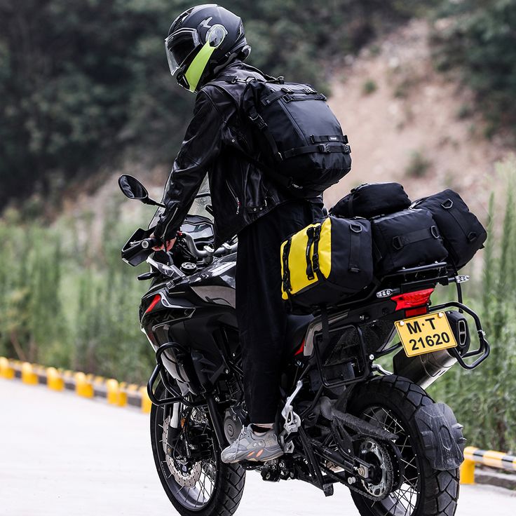Motorcyclist on a road trip with gear bags, wearing a helmet and jacket, riding a loaded adventure bike.