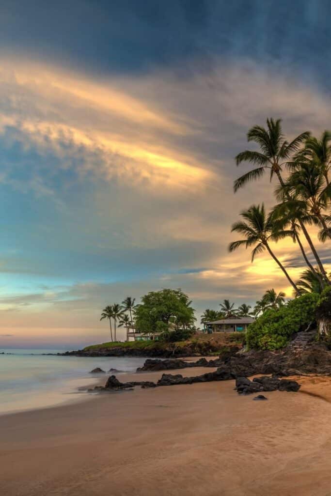 Tropical beach at sunset with palm trees, calm ocean waves, and vibrant sky in a peaceful coastal landscape.