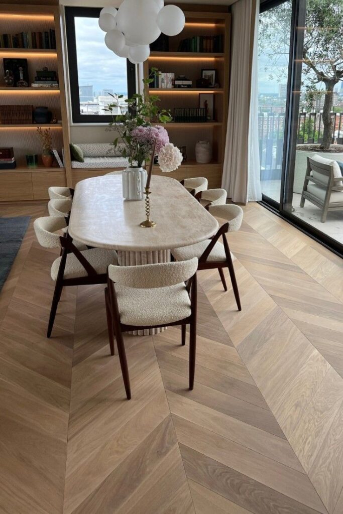 Modern dining room with marble table, elegant chairs, bookshelf, and large window overlooking a scenic view.