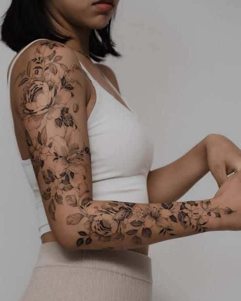 Woman with detailed floral arm tattoos in white top, showcasing elegant ink design.