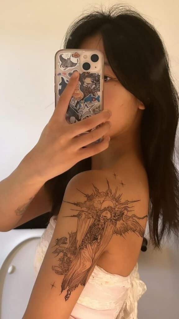 Woman taking a mirror selfie showcasing a detailed shoulder tattoo depicting a celestial scene, using a smartphone.