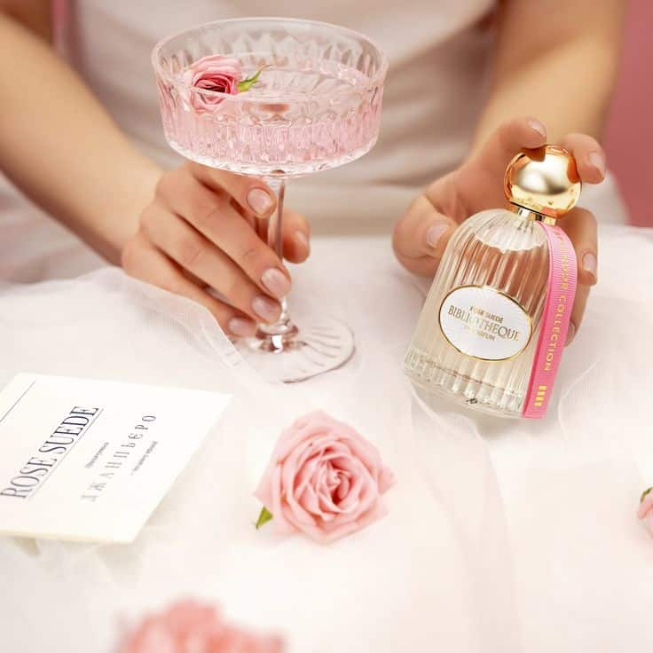 Elegant setting with pink cocktail, perfume bottle, and roses on tulle, evoking luxury and romance.