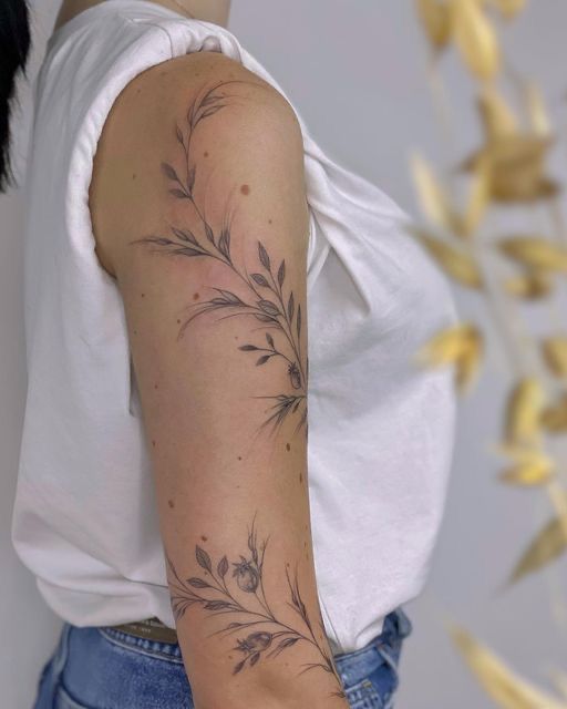 Floral arm tattoo on a person wearing a white top and jeans, soft focus on background.
