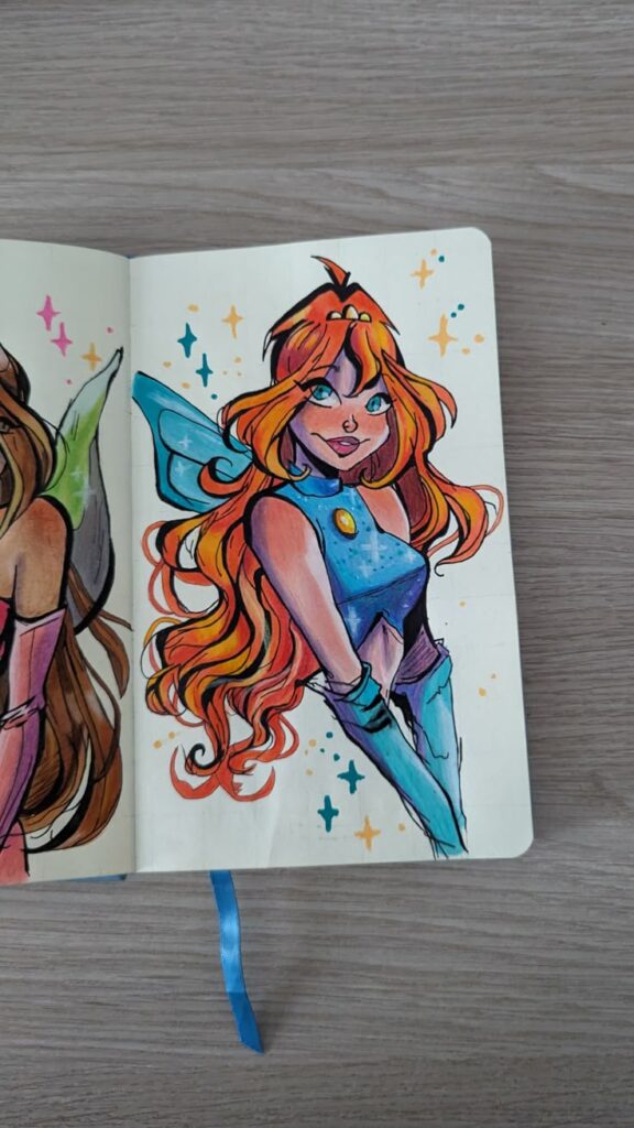 Colorful sketch of a fairy with blue wings and orange hair in a notebook, surrounded by sparkling stars.