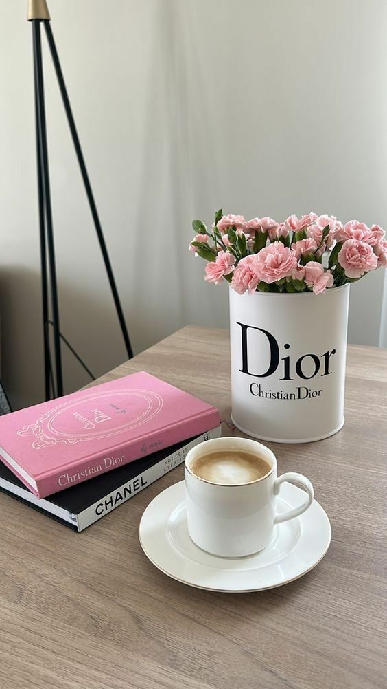 Coffee cup on table with Dior flowers and fashion books for a stylish, cozy atmosphere.