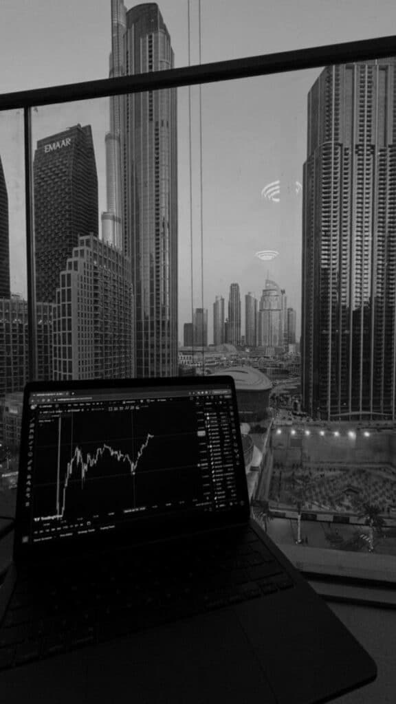 Laptop displaying stock chart with city skyscrapers view from window.