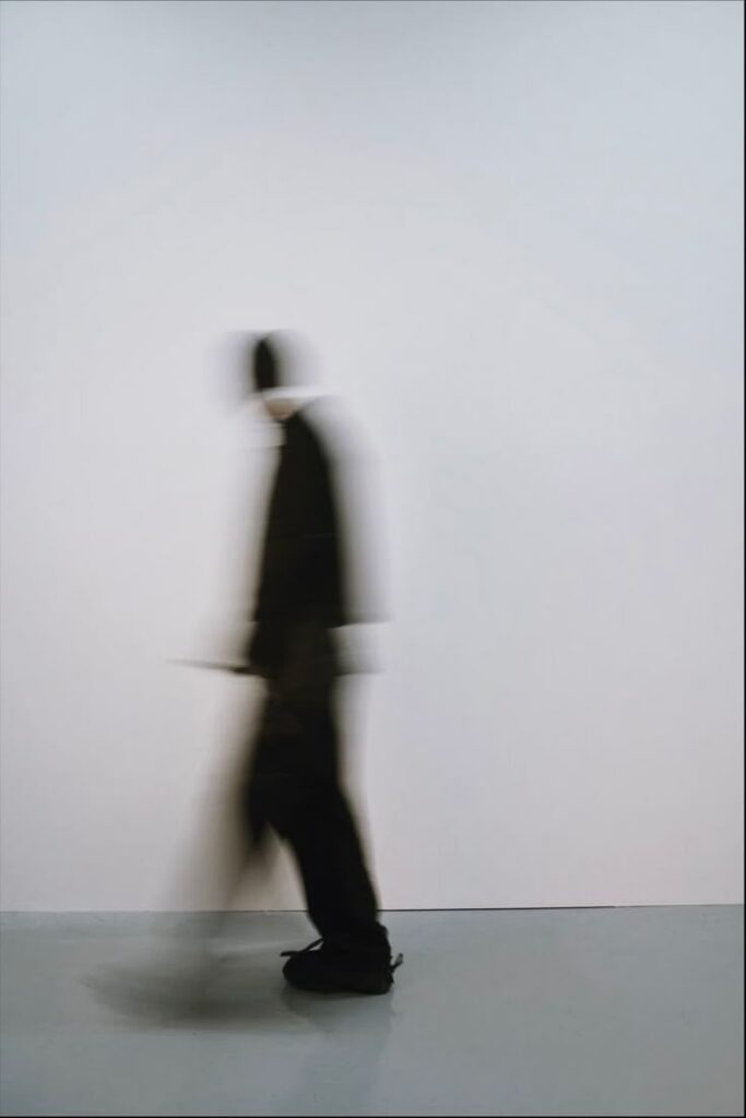 Blurred silhouette of a person walking in motion against a minimalist background.