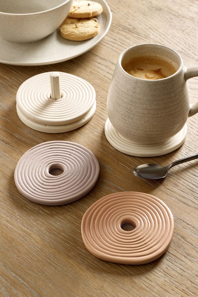Ceramic cup with coffee, round coasters, cookies, and a spoon on a wooden table for a cozy breakfast setting.