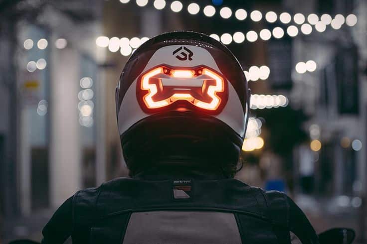 Motorcyclist with illuminated smart helmet riding at night with blurred city lights in background.
