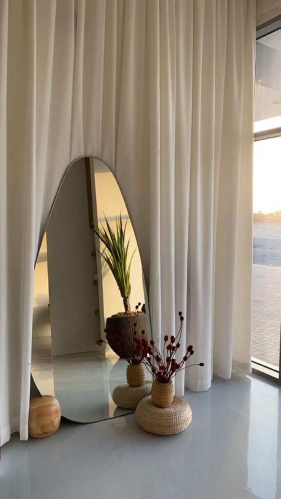 c759acc4-6bbb-41c1-87df-4bfbb06e4087 Modern interior with oval mirror, white curtains, and decorative plants on a smooth floor, showcasing minimalist design. | Sky Rye Design Modern interior with oval mirror, white curtains, and decorative plants on a smooth floor, showcasing minimalist design.