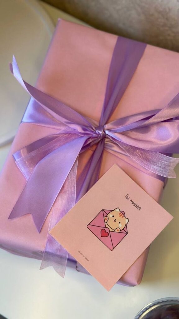 Pink gift box with a purple ribbon and a cute cat card, perfect for special occasions.