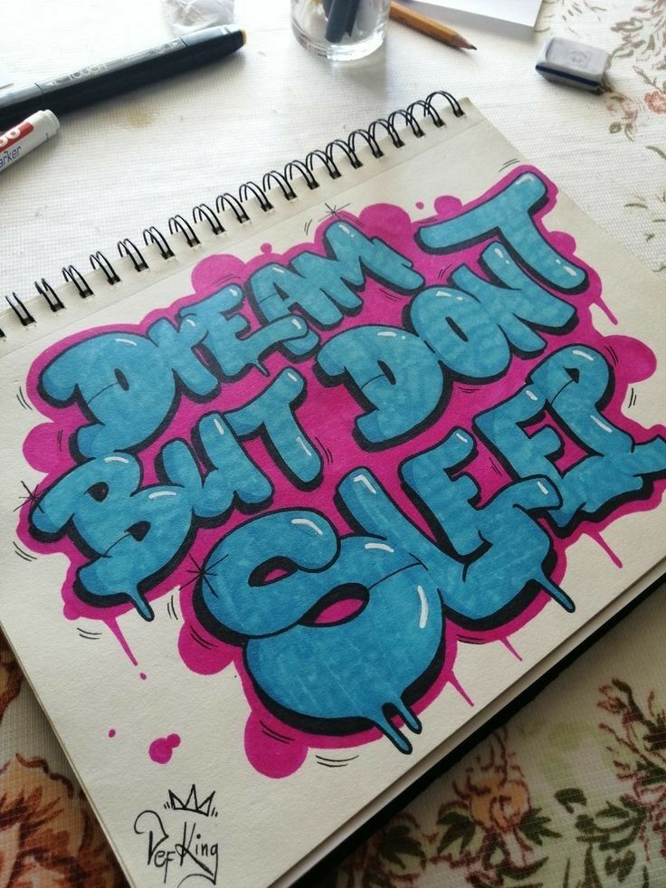 Graffiti-style text on notebook reads Dream but don't sleep in blue and pink, surrounded by art supplies.
