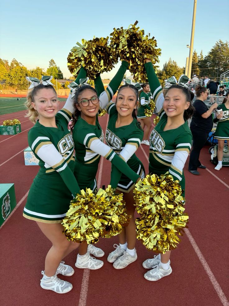 Cheerleaders in green uniforms with pom-poms smile on a track field, showcasing team spirit and enthusiasm.