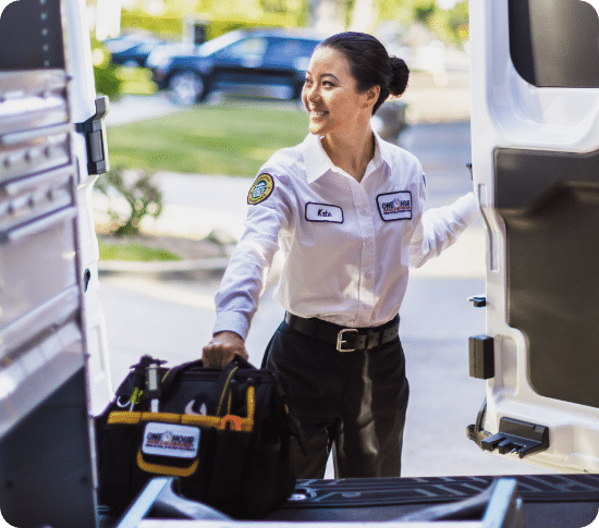 Female technician with a tool bag exiting a service van, wearing a branded uniform and smiling confidently.