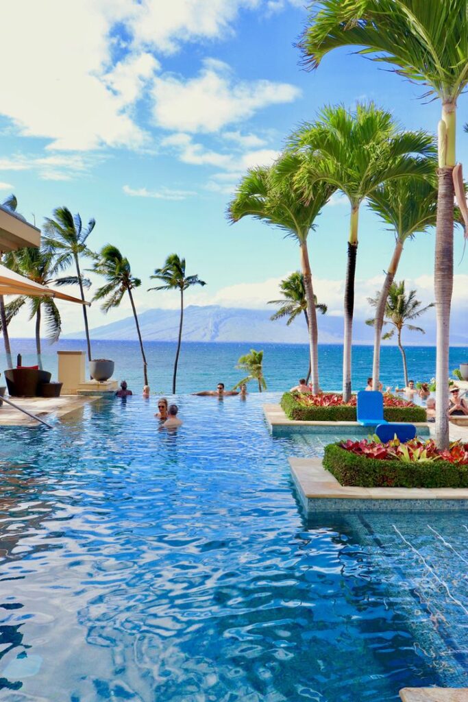 Luxury infinity pool overlooking the ocean, surrounded by palm trees and clear blue sky. Perfect tropical getaway.