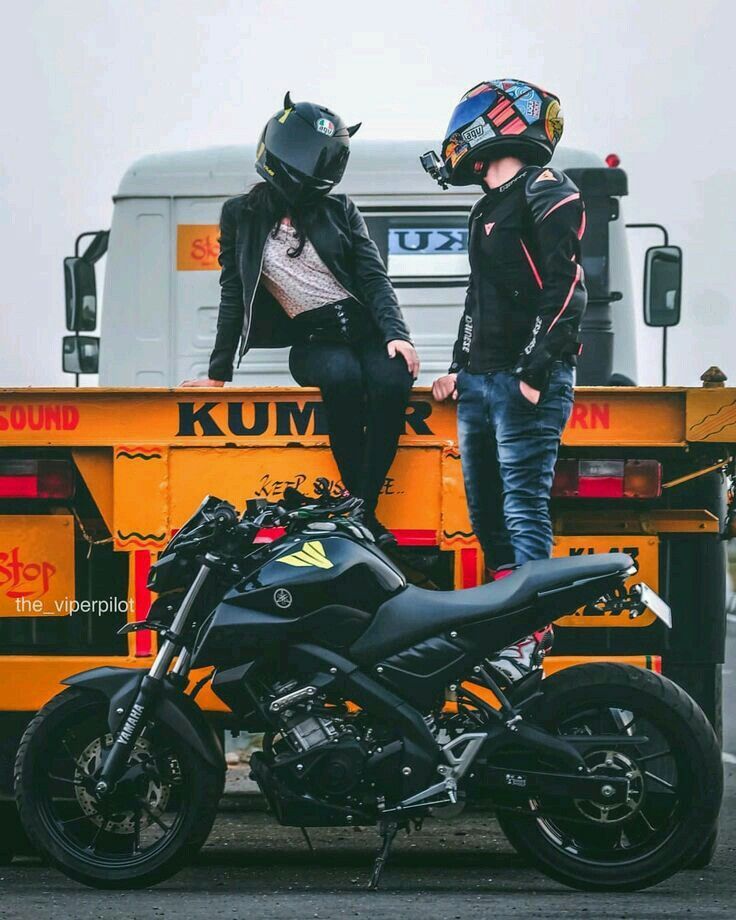 Two people in motorcycle gear pose with a black sports bike next to a truck on a road.